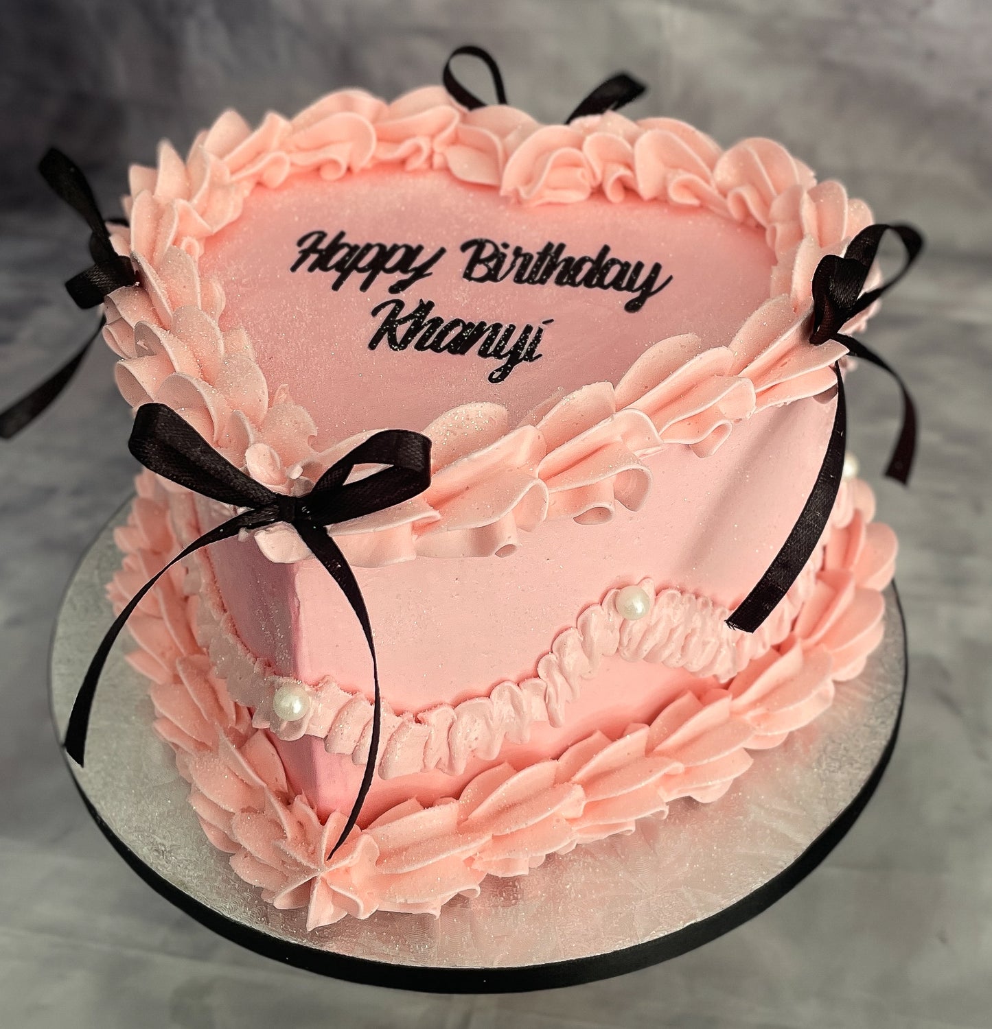 Pink birthday cake with ruffles and black ribbons on a gray background