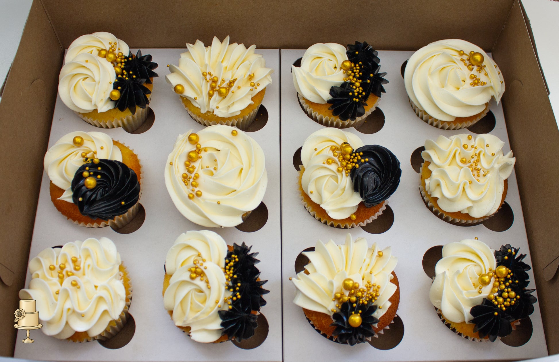 Decorative cupcakes with white, black, and gold frosting in a box.